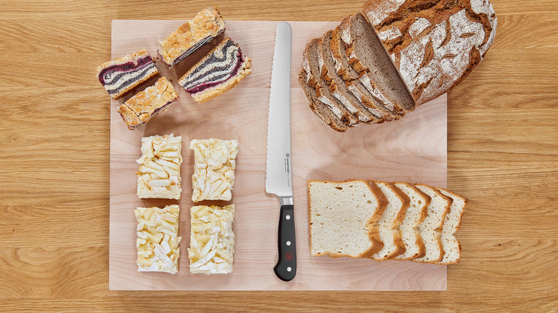 Classic 10" Super Slicer with a serrated German steel blade and triple-riveted handle placed on a board with sliced bread and assorted pastries.