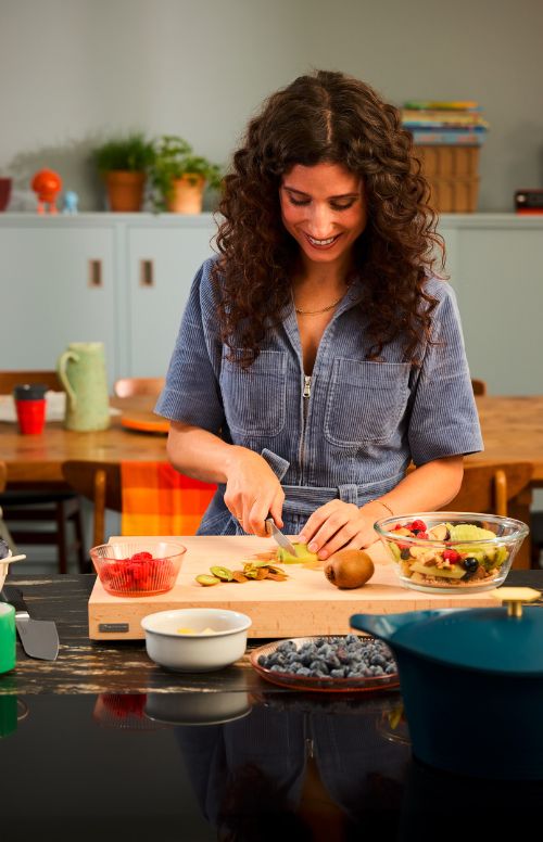 Woman preparing a salad in a kitchen with various ingredients on the counter.
