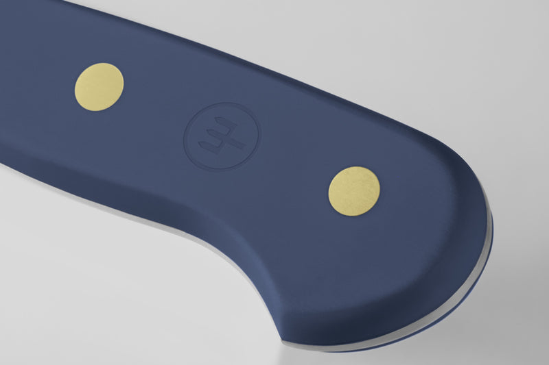 Close-up of the rounded heel on the Classic 5" Serrated Utility Knife with a matte blue handle featuring two brass rivets and a subtle embossed logo.
