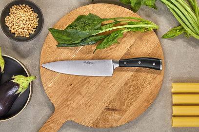 Wooden cutting board with a knife, surrounded by vegetables on a gray surface