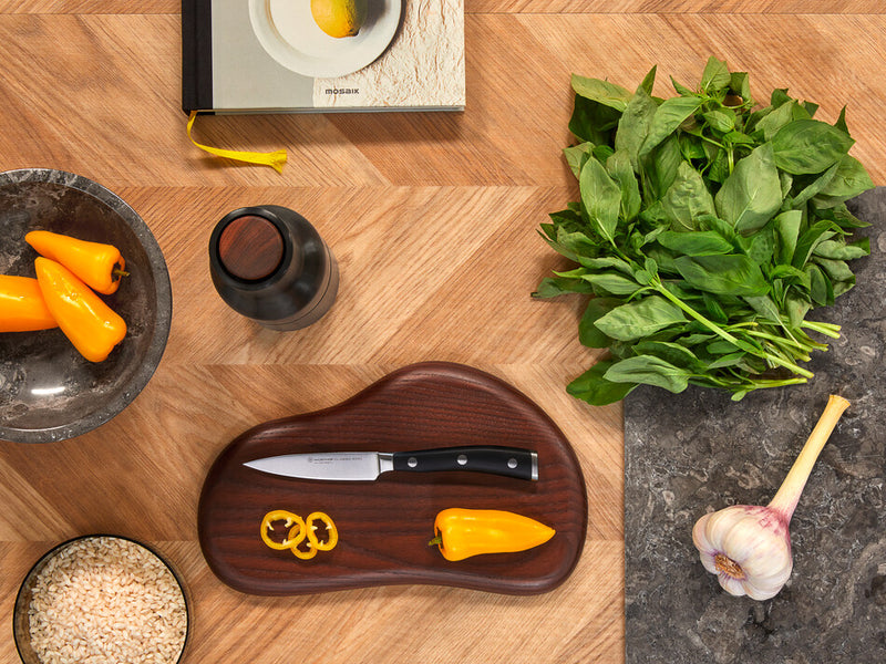 Classic Ikon 3 1/2" Paring Knife with a forged German steel blade and triple-riveted black handle placed on a wooden board with sliced yellow pepper.