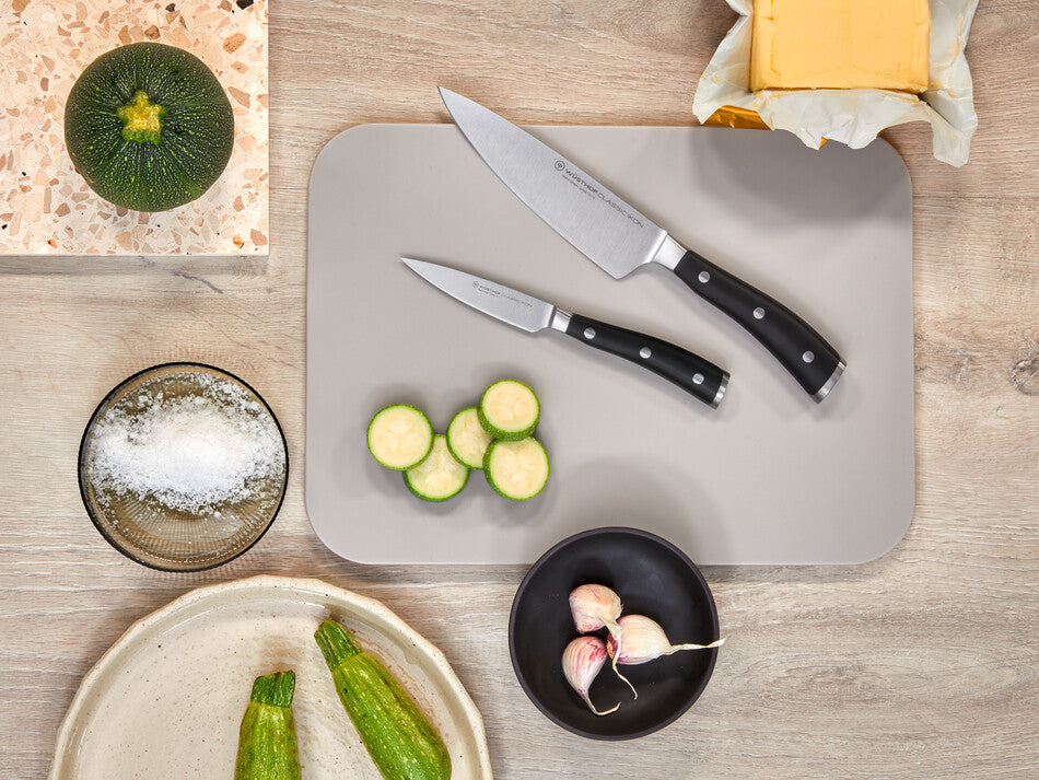 Classic Ikon 2-Piece Cook's Set with forged German steel chef's and paring knives featuring black ergonomic handles displayed on a gray cutting board.