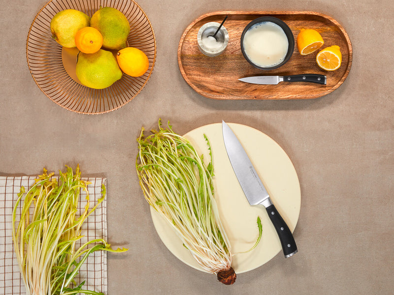 Classic Ikon 2-Piece Cook's Set featuring a forged German steel chef’s knife with black ergonomic handle displayed on a beige plate with fresh bean sprouts.