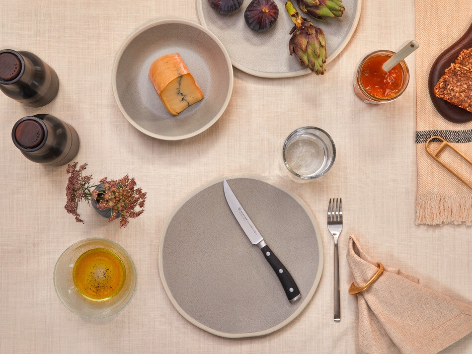 Classic Ikon 4 1/2" Steak Knife with a finely forged German steel blade and a triple-riveted black handle displayed on a neutral table setting.