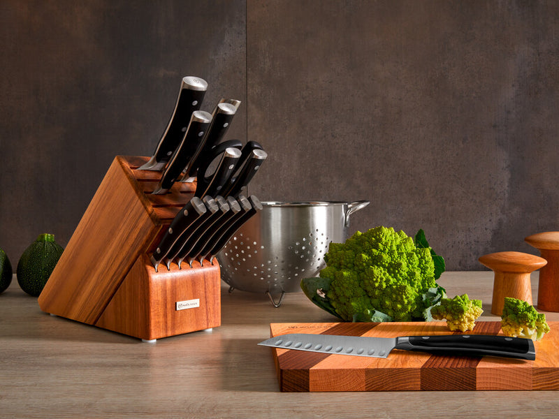 Classic Ikon 15-Piece Knife Block Set featuring forged kitchen knives with triple-riveted black handles displayed alongside fresh vegetables and a stainless steel colander.