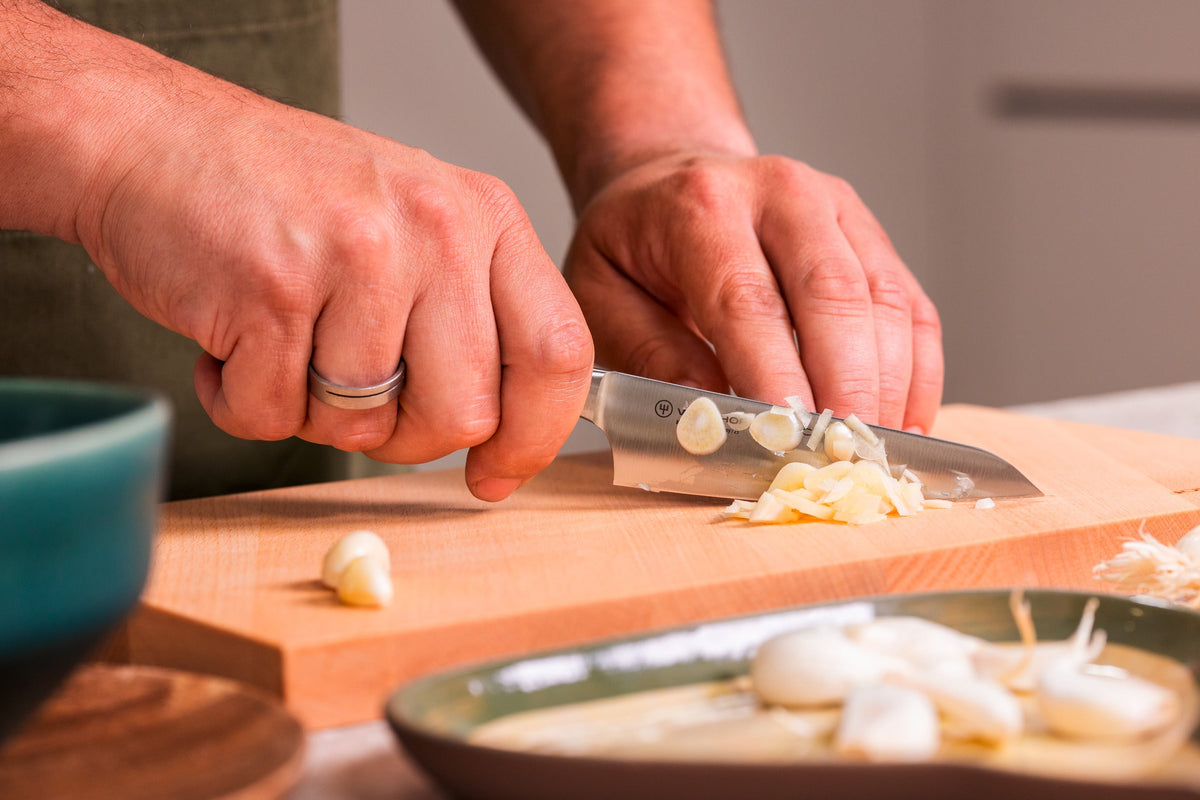 Classic 2-Piece Asian Knife Set in use chopping garlic on a wooden cutting board with focus on the forged German blade and comfortable grip.