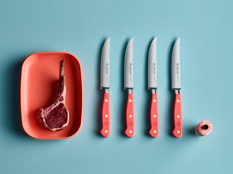 Classic 4-Piece Steak Knife Set with bright coral handles featuring full tang construction and triple brass rivets, displayed next to a raw ribeye steak.