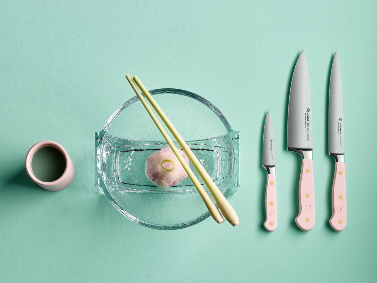 Classic 6" Chef's Knife set with forged German steel blades and pale pink handles featuring brass rivets, displayed alongside chopsticks and a garlic bulb.