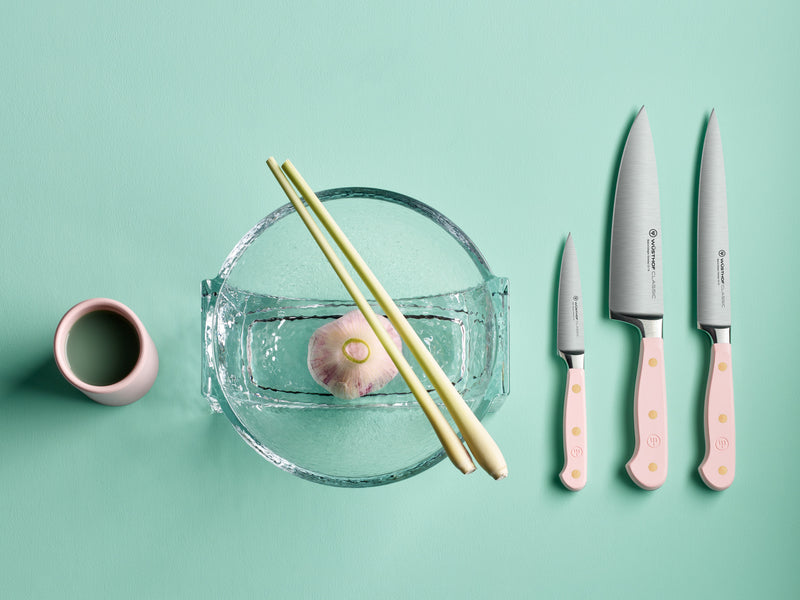 Classic 6" Chef's Knife set with forged German steel blades and pale pink handles featuring brass rivets, displayed alongside chopsticks and a garlic bulb.