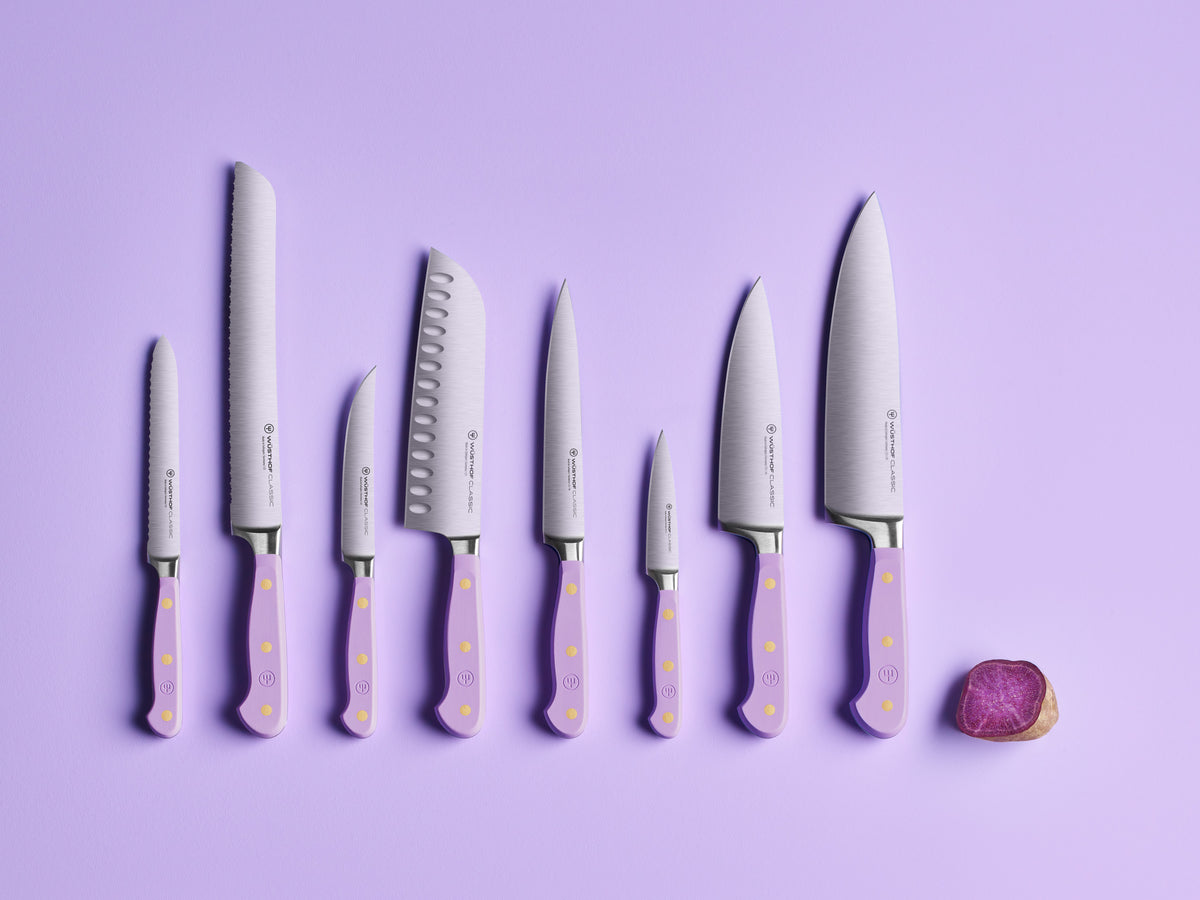 Classic 8" Chef's Knife paired with a set of forged German steel kitchen knives featuring lavender handles and brass rivets, displayed on a purple background with a sliced purple vegetable.