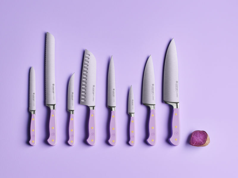 Classic 8" Chef's Knife paired with a set of forged German steel kitchen knives featuring lavender handles and brass rivets, displayed on a purple background with a sliced purple vegetable.