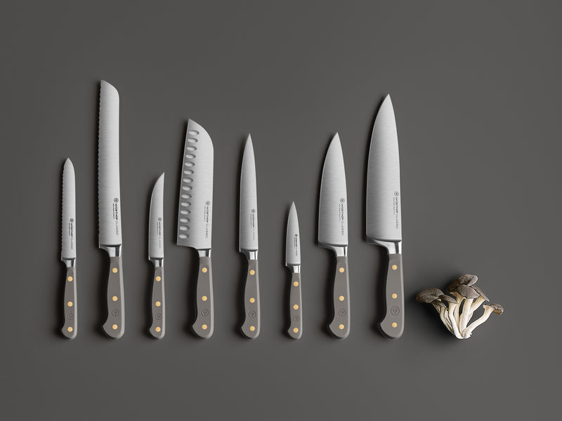 Classic 8" Chef's Knife displayed among a matching set of forged German knives with dark handles and brass rivets, alongside fresh mushrooms on a grey background.