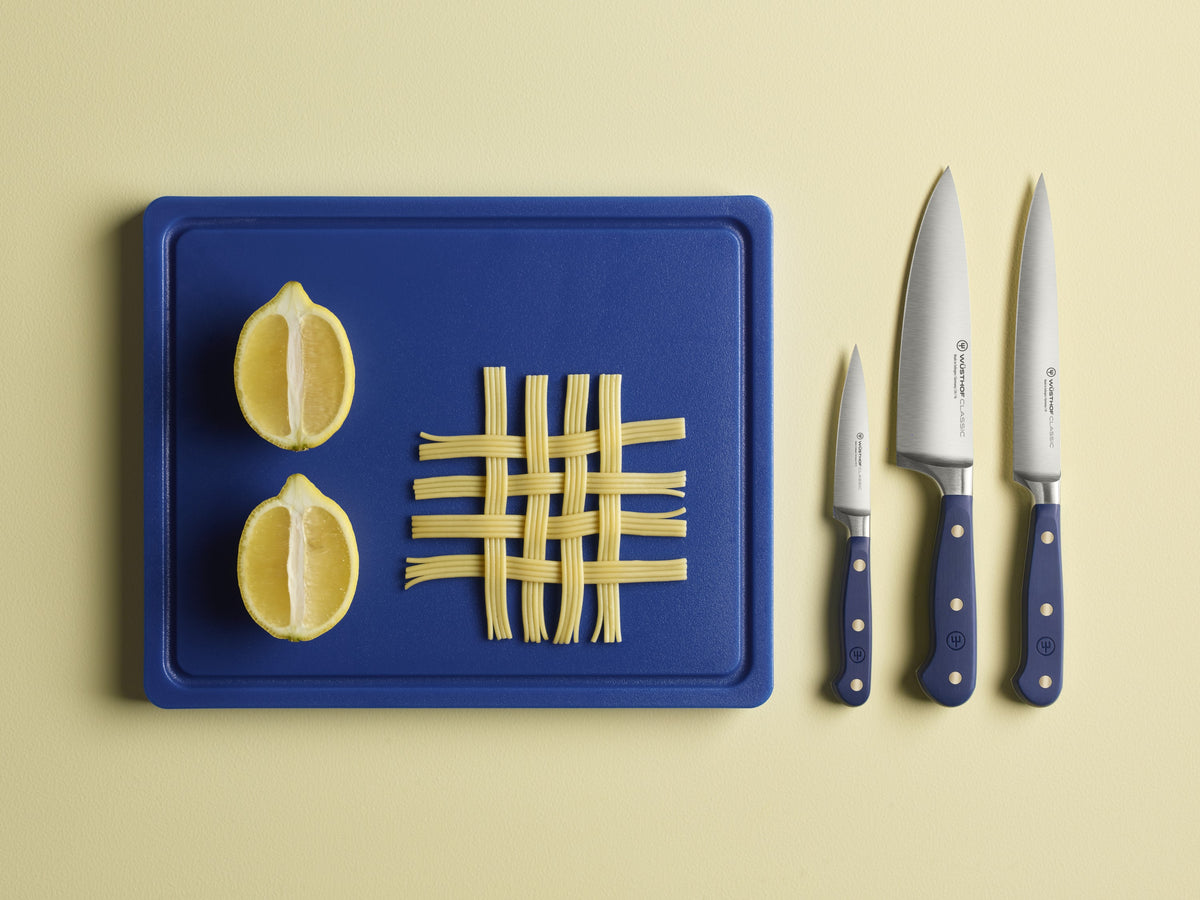 Classic 6" Utility Knife set with navy ergonomic handles and brass rivets displayed next to a blue cutting board holding two lemon halves and crossed dry pasta strands.