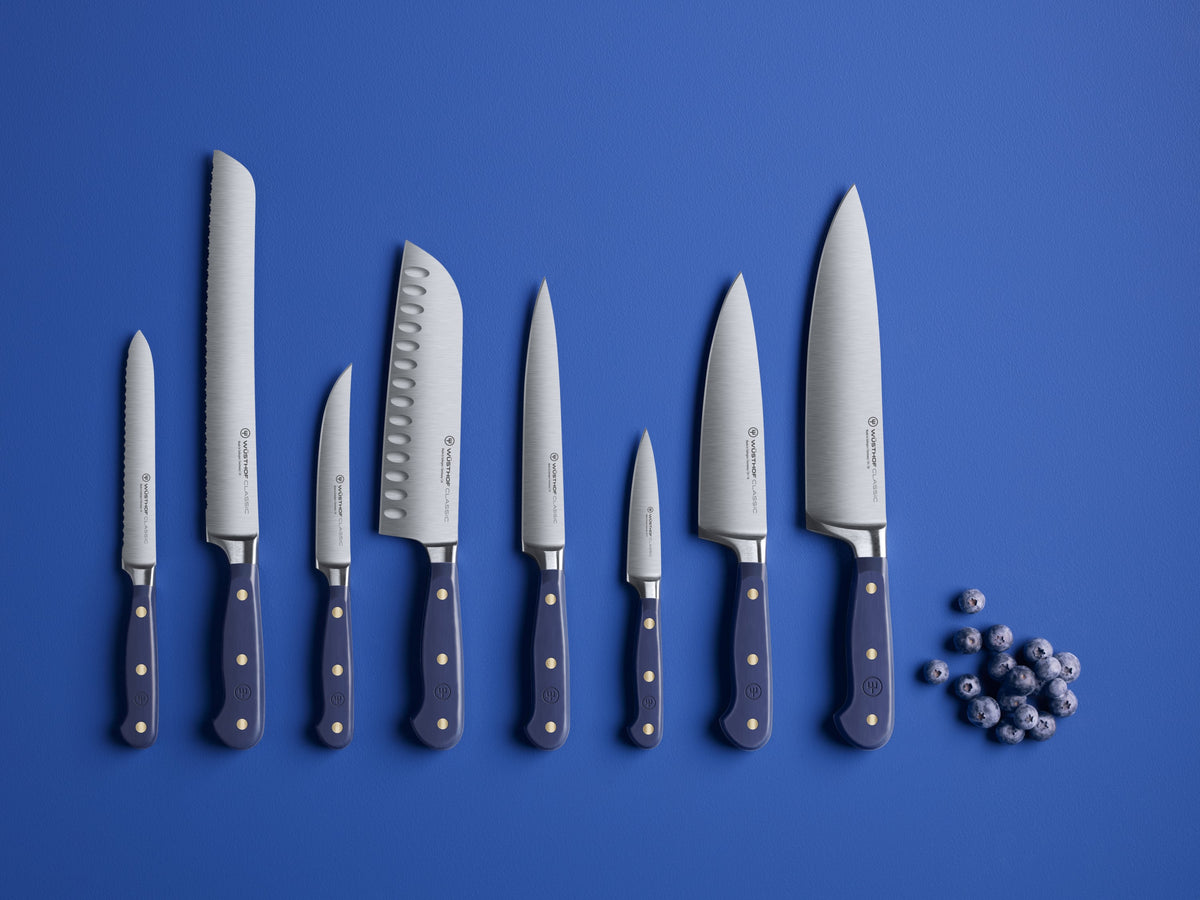 Classic 8-Piece Designer Knife Block Set displayed with forged German steel blades and dark ergonomic handles featuring brass rivets against a blue background.