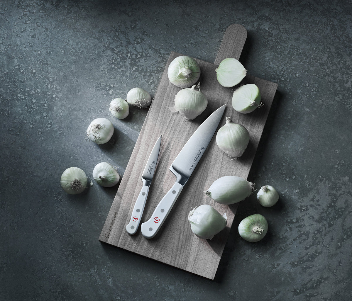 Classic 3 1/2" Paring Knife with a polished forged German steel blade and smooth white handle with three rivets, displayed on a wooden cutting board with peeled onions.