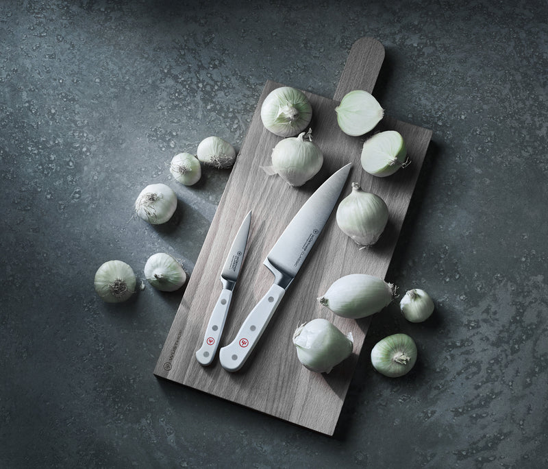 Classic 3 1/2" Paring Knife with a polished forged German steel blade and smooth white handle with three rivets, displayed on a wooden cutting board with peeled onions.