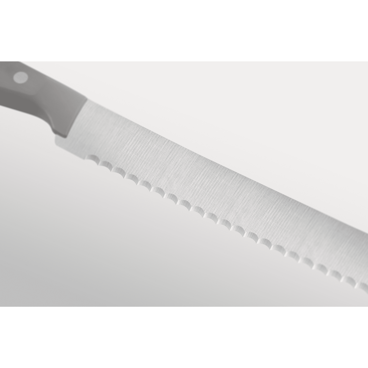 Close-up of a serrated forged German kitchen knife blade with a grey ergonomic handle, part of the Gourmet Grey 3-Piece Starter Set.