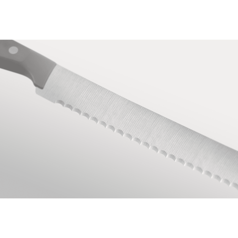 Close-up of a serrated forged German kitchen knife blade with a grey ergonomic handle, part of the Gourmet Grey 3-Piece Starter Set.