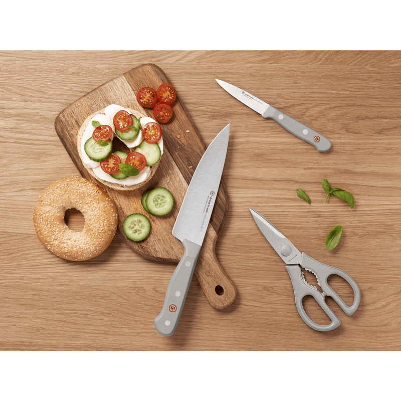 Overhead view of the Gourmet Grey 3-Piece Essentials Set featuring forged German knives with grey handles and kitchen shears beside a sliced bagel with cucumber and cherry tomatoes.