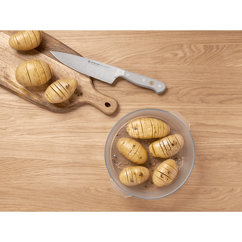 Top view of a forged German chef's knife with a grey handle from the Gourmet Grey 3-Piece Essentials Set alongside scored potatoes on a wooden surface.