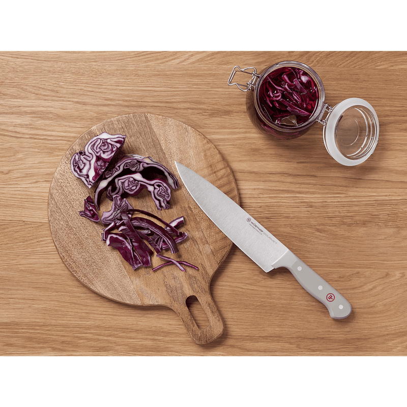 Top view of a sliced purple cabbage on a round wooden cutting board alongside a forged German chef's knife with a grey ergonomic handle from the Gourmet Grey 3-Piece Chef's Set.