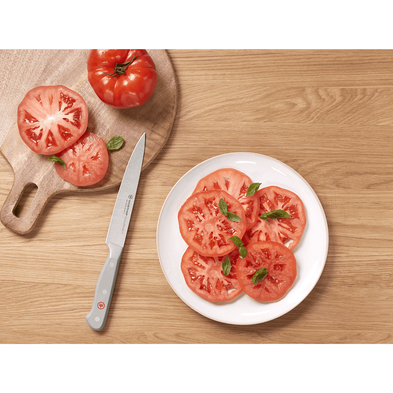 Sliced tomatoes on a wooden cutting board and white plate with fresh basil, next to a forged German knife with a grey handle from the Gourmet Grey 3-Piece Chef's Set.