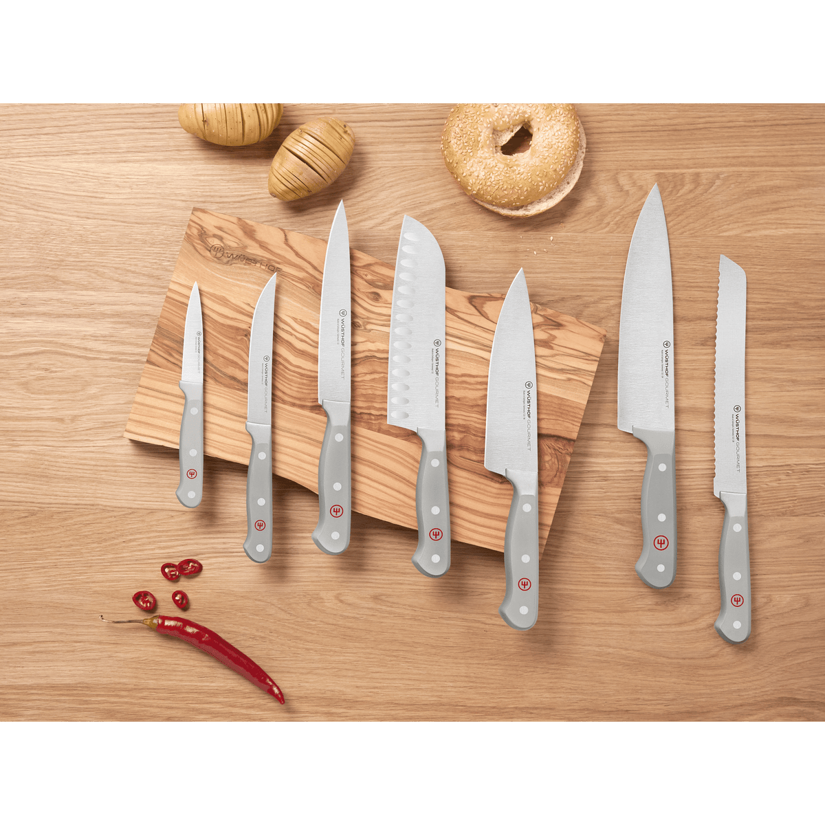 Arrangement of forged WÜSTHOF kitchen knives with grey handles on a wooden surface and cutting board, highlighting the Gourmet Grey 4-Piece Starter Set among other knives.