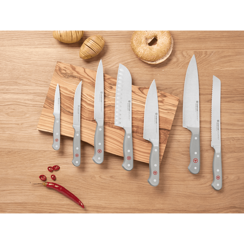 Arrangement of forged WÜSTHOF kitchen knives with grey handles on a wooden surface and cutting board, highlighting the Gourmet Grey 4-Piece Starter Set among other knives.