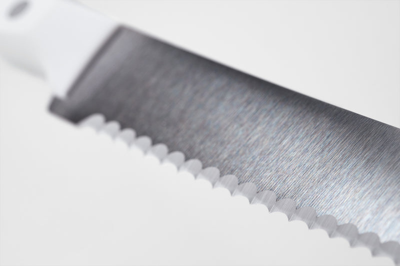 Close-up of a serrated forged German blade with a sharp edge and white ergonomic handle from the Gourmet 16-Piece Knife Block Set.