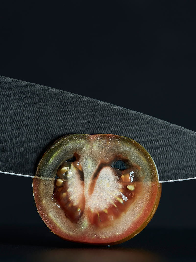 Performer 6" Chef's Knife cutting through a ripe heirloom tomato, showcasing its sharp forged German steel blade and precision edge.