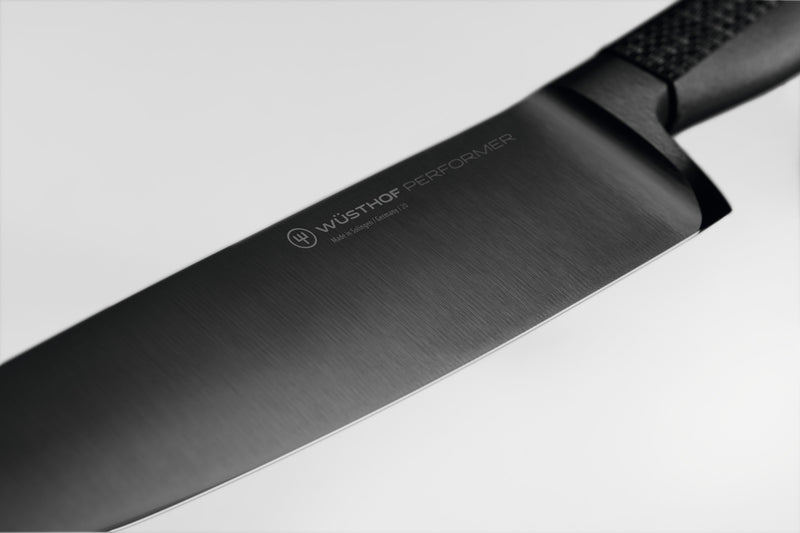 Performer 6" Chef's Knife featuring a finely forged black German steel blade with subtle branding and a textured handle for superior control.