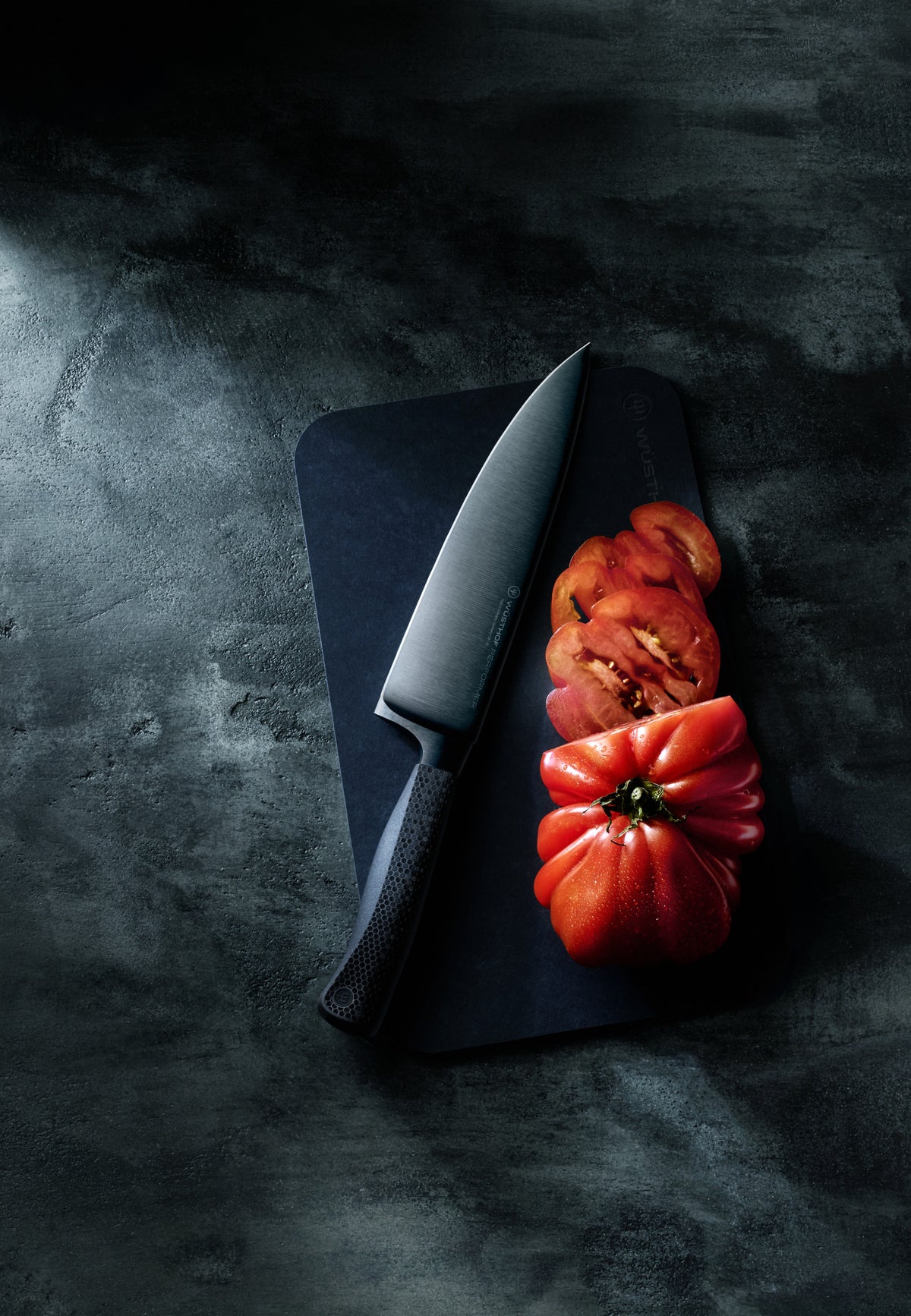 Performer 8" Chef's Knife cutting a fresh heirloom tomato on a dark cutting board, showcasing its sharp forged German steel blade and textured handle.