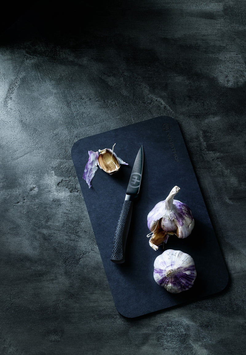 Performer 3 1/2" Paring Knife with a textured ergonomic handle and sharp forged blade resting on a cutting board beside whole and peeled garlic cloves.