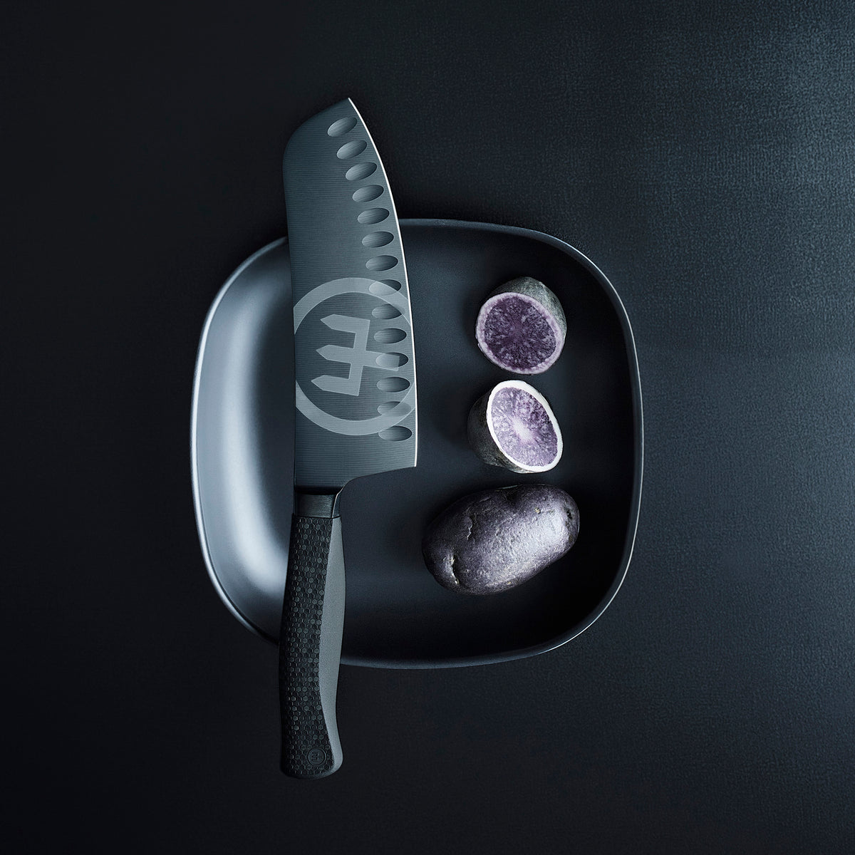 Performer 7" Hollow Edge Rotoku featuring a dark blade with hollow indentations and textured handle displayed on a black plate with purple potatoes.