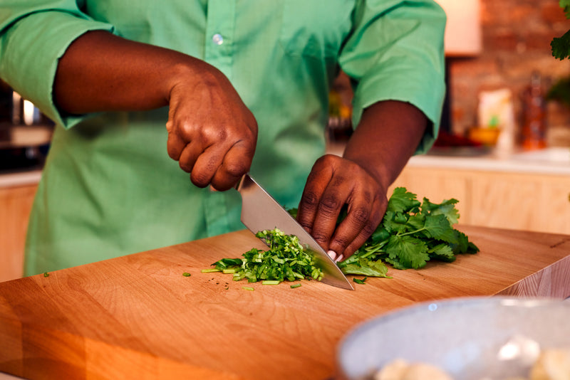 Partner 7-Piece Knife Block Set featuring a forged German chef’s knife chopping fresh herbs on a wooden cutting board in a home kitchen setting.
