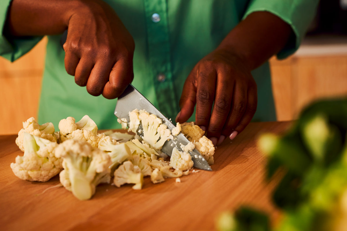 Partner 7-Piece Knife Block Set showing a forged German kitchen knife with a black ergonomic handle cutting fresh cauliflower on a wooden board.