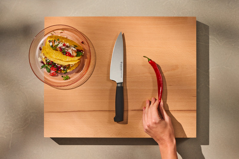 Partner 7-Piece Knife Block Set showcasing a forged German chef’s knife with a smooth black handle on a wooden cutting board alongside a fresh red chili and prepared tacos.