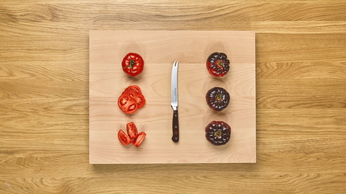 Classic 5" Tomato Knife with a dark wooden handle and a curved serrated stainless steel blade, displayed on a wooden cutting board with red and purple tomato slices.