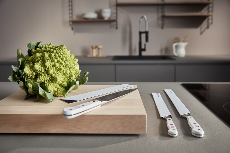 Classic 8" Chef's Knife with a white handle resting on a wooden cutting board next to a fresh Romanesco broccoli in a modern kitchen setting.