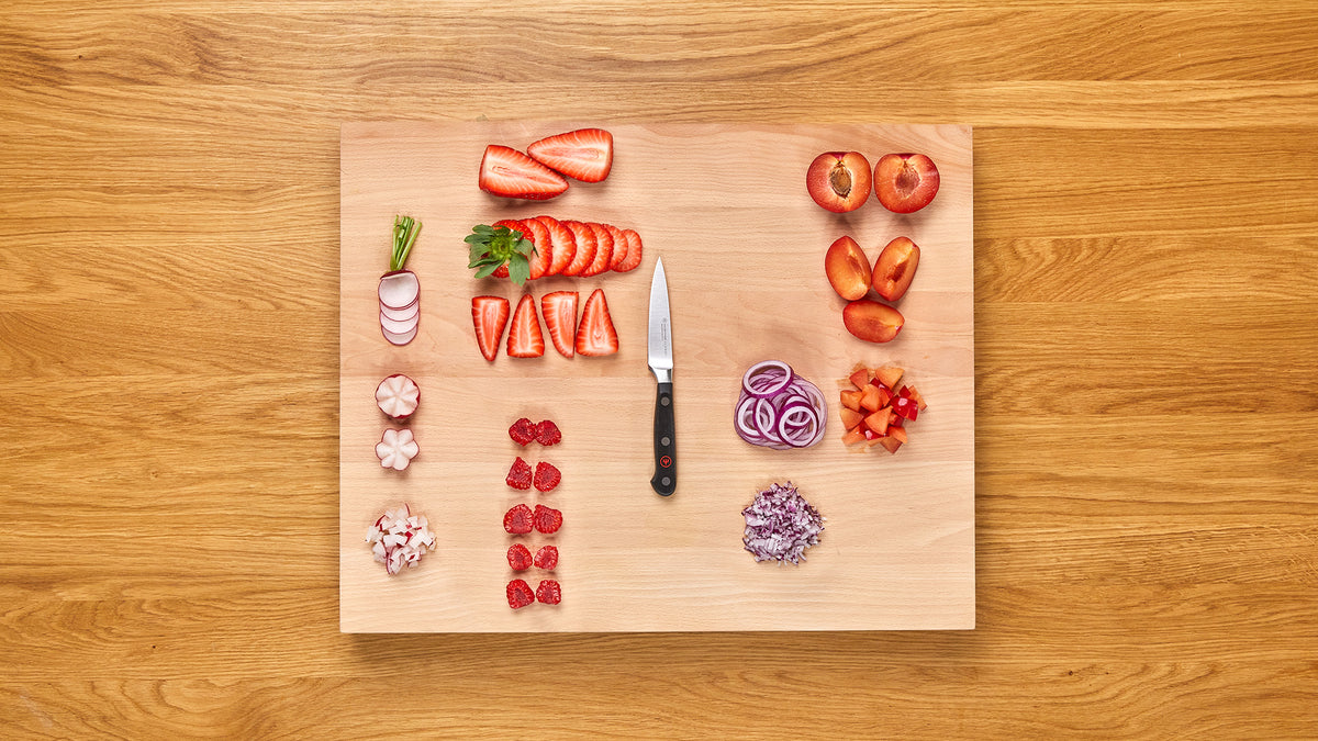 Classic 3 1/2" Paring Knife with a sleek black handle and stainless steel rivets, displayed on a wooden cutting board with neatly chopped strawberries, radishes, onions, and plums.