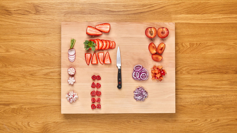 Classic 3 1/2" Paring Knife with a sleek black handle and stainless steel rivets, displayed on a wooden cutting board with neatly chopped strawberries, radishes, onions, and plums.