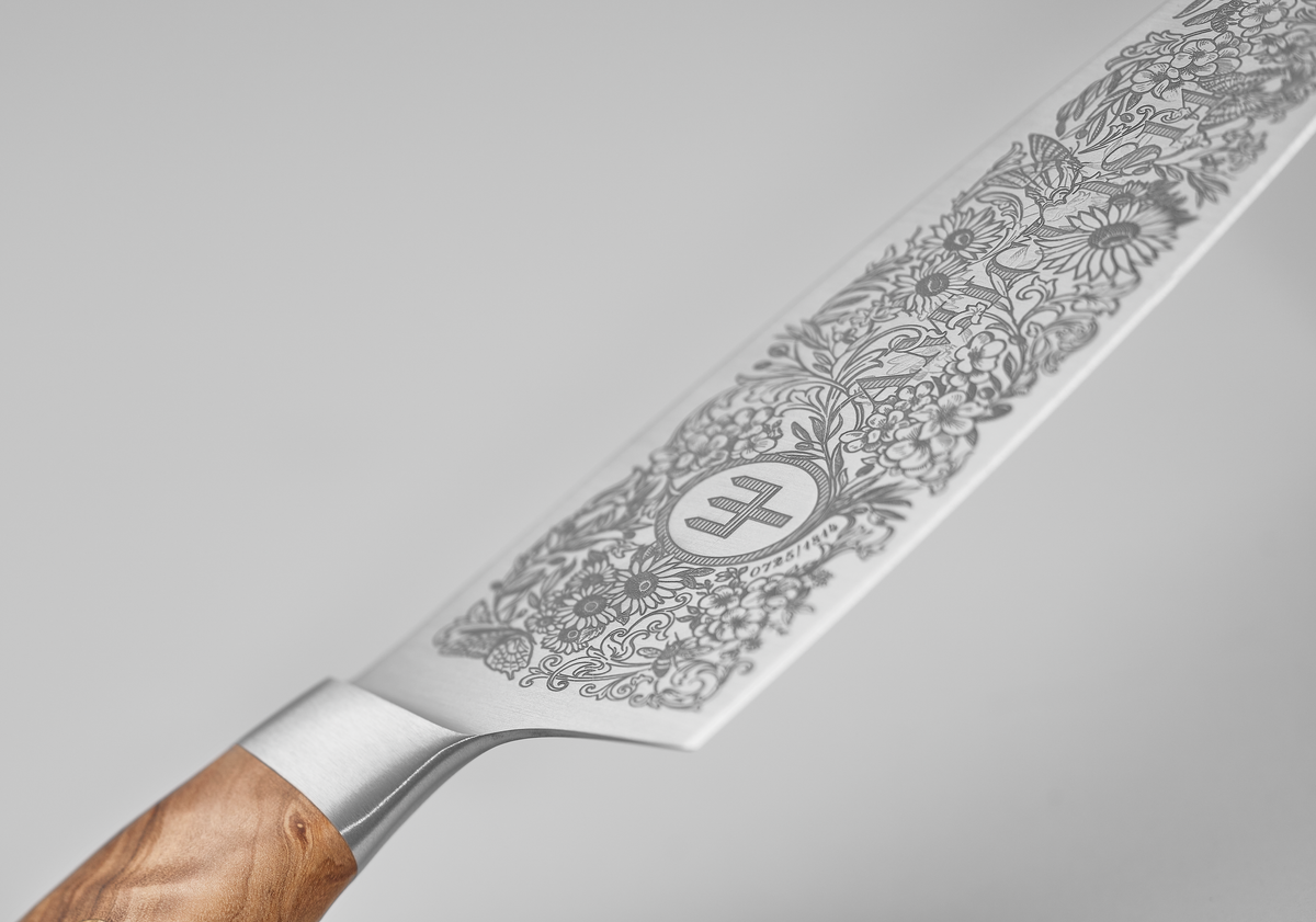 Amici 1814 forged kitchen knife blade featuring an ornate floral etching with a central emblem and a polished wooden handle.