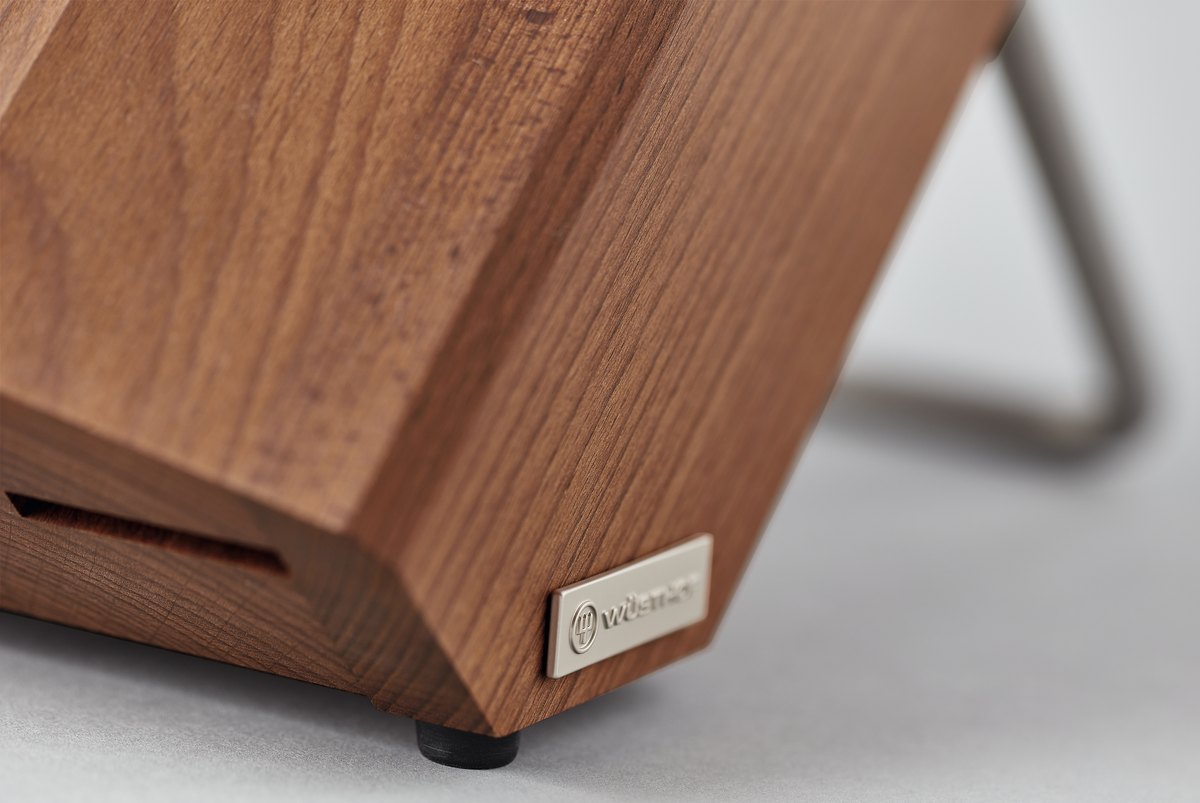 Close-up of the corner of the 8-Slot Heat Treated Beech Knife Block showing smooth wood grain, precise joinery, and a metal logo plate on a stable base.