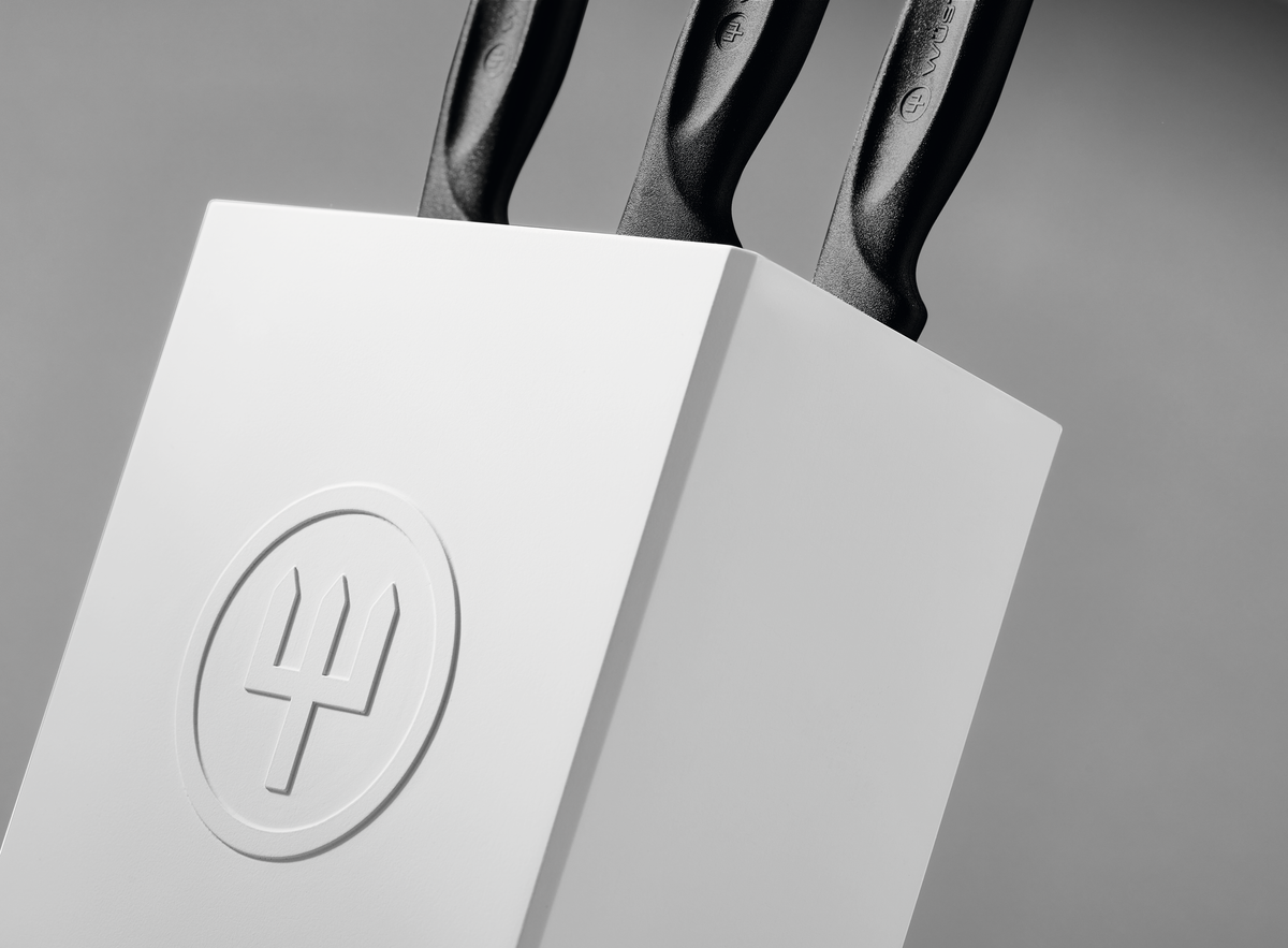 Create Knife Block close-up showing a minimalist white holder with embossed logo securing three black-handled forged German knives.