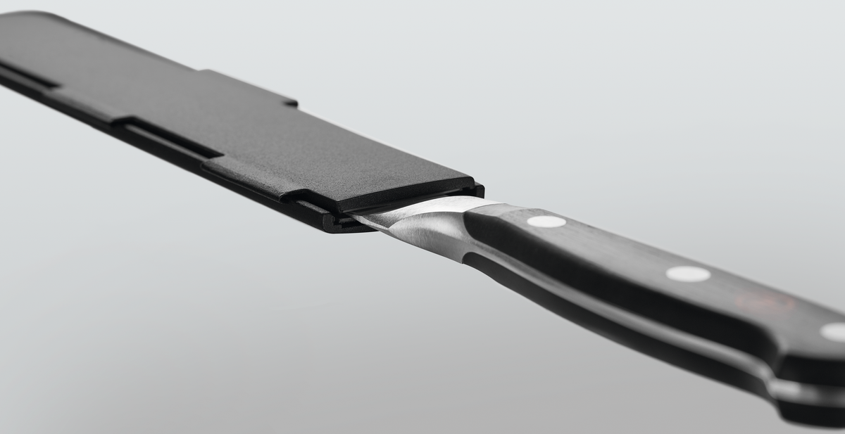 Narrow Magnetic Blade Guard in black securely enclosing the blade of a forged kitchen knife with a polished black handle and metal rivets for safe storage.
