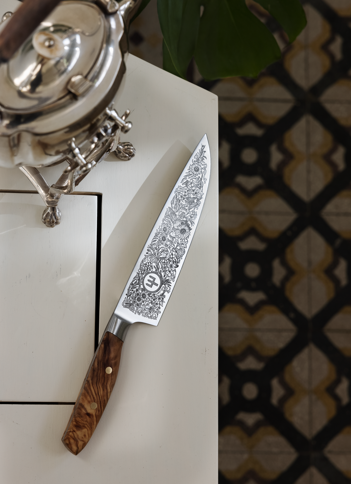 Amici 1814 forged kitchen knife featuring detailed floral etchings on the blade and a polished olive wood handle with brass rivets.