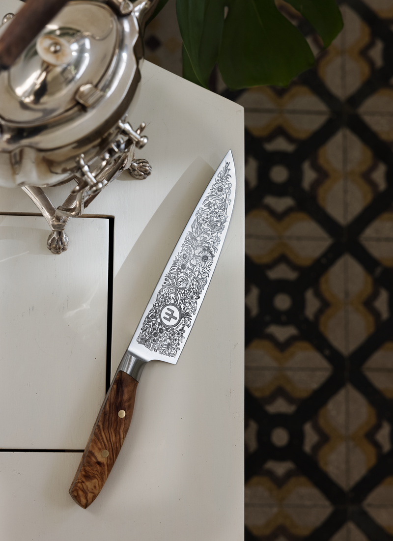 Amici 1814 forged kitchen knife featuring detailed floral etchings on the blade and a polished olive wood handle with brass rivets.