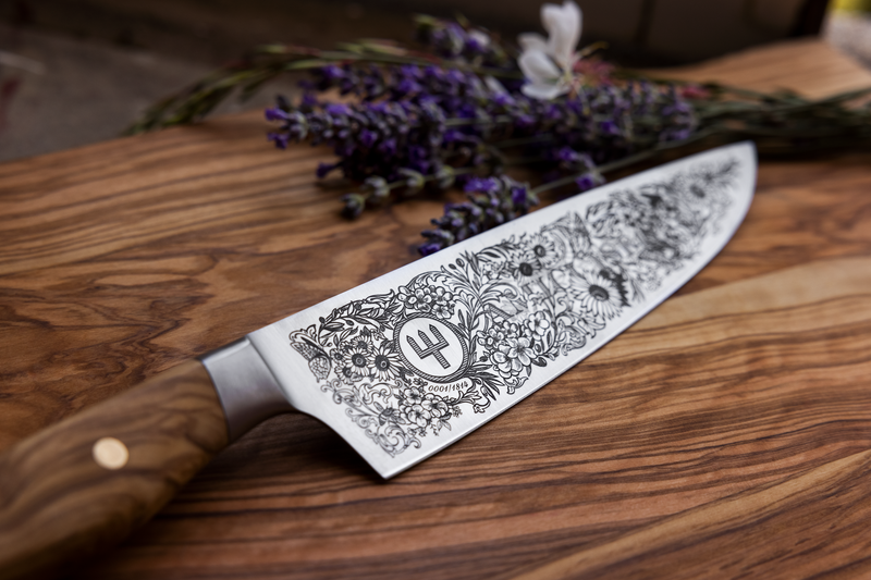 Amici 1814 forged kitchen knife blade with intricate floral and botanical engravings and a smooth olive wood handle with brass rivets.