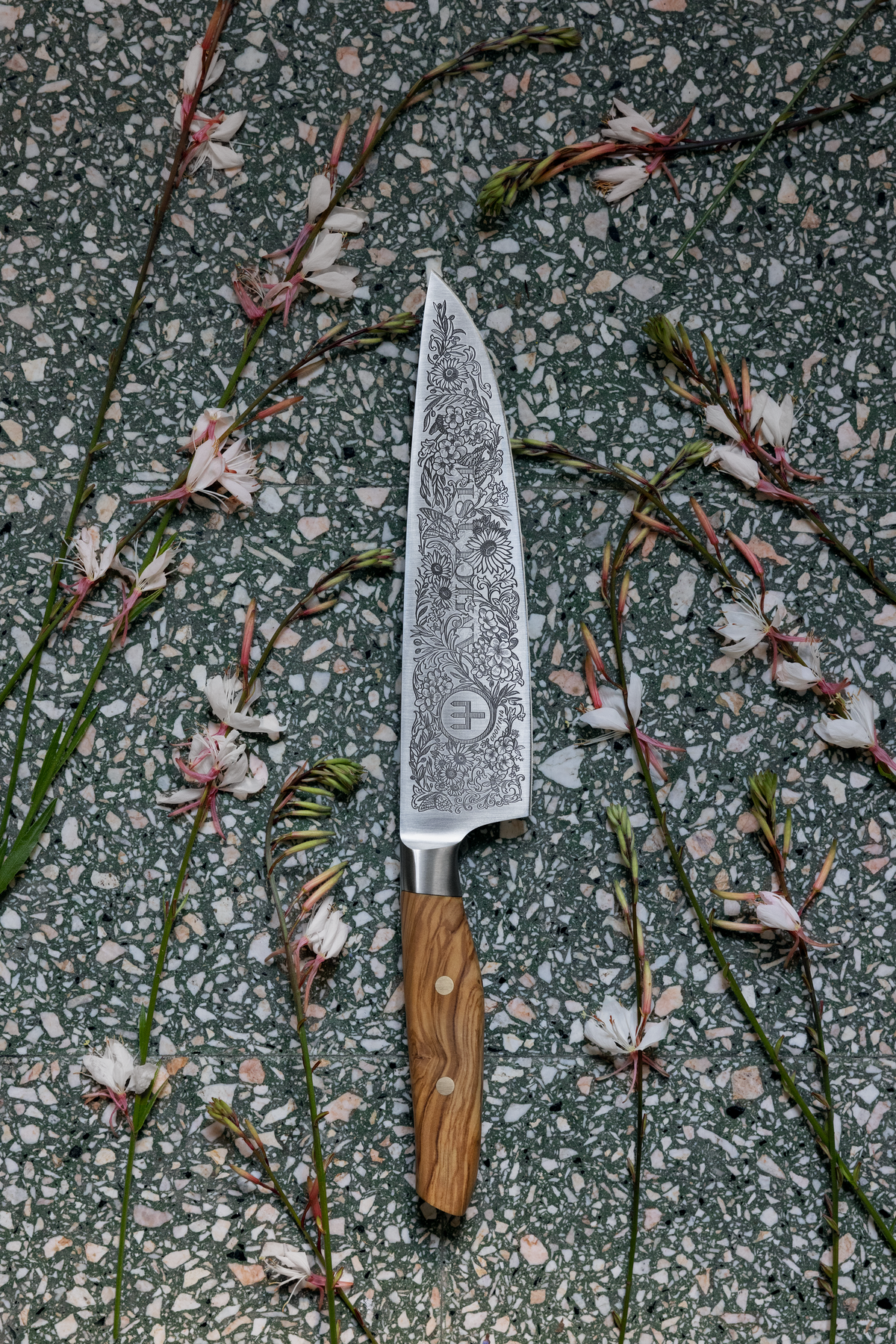 Amici 1814 forged kitchen knife with finely detailed floral engravings on the blade and a smooth olive wood handle with brass rivets.