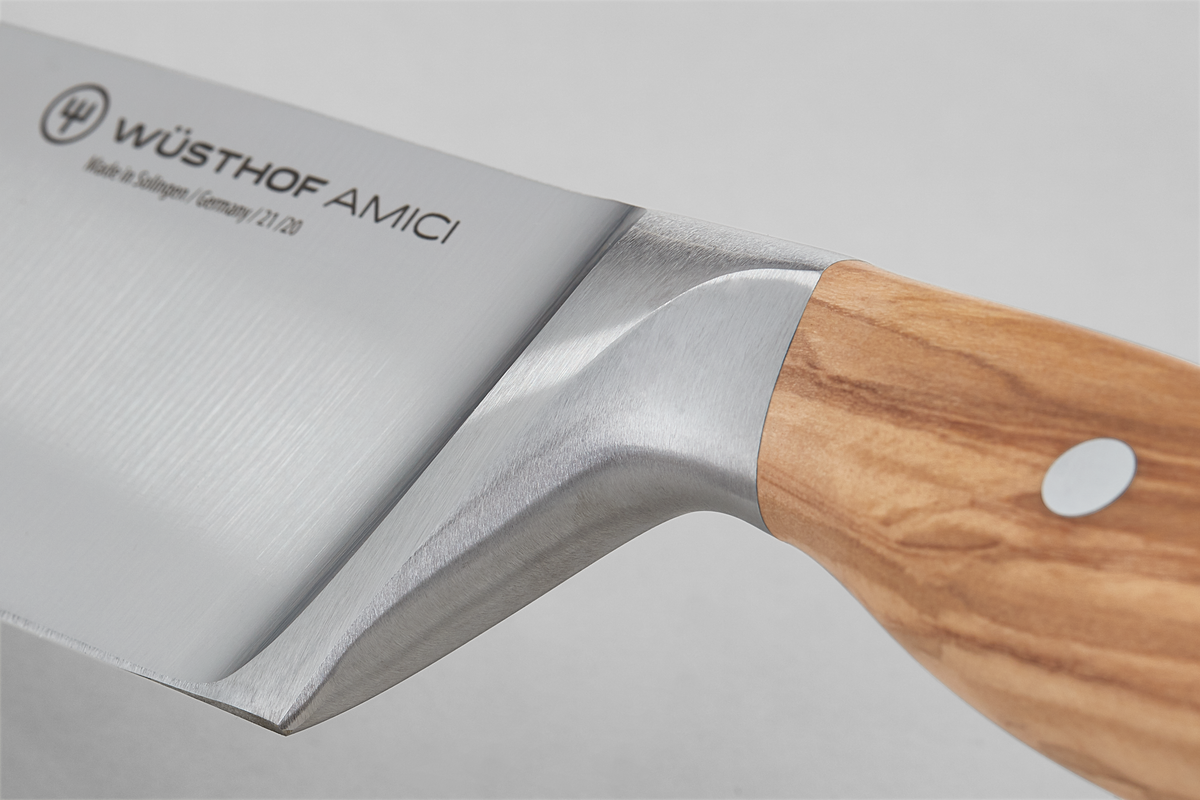 Close-up of the full bolster transition between the forged stainless steel blade and the light olive wood handle on the "Amici 8" Chef's Knife.